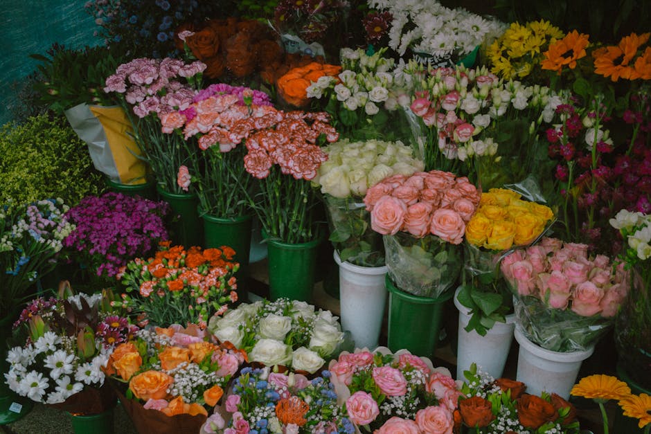 A vibrant display of fresh floral arrangements in various colors and styles, including roses in shades of pink, yellow, and white, as well as carnations, daisies, and chrysanthemums in pink, purple, o